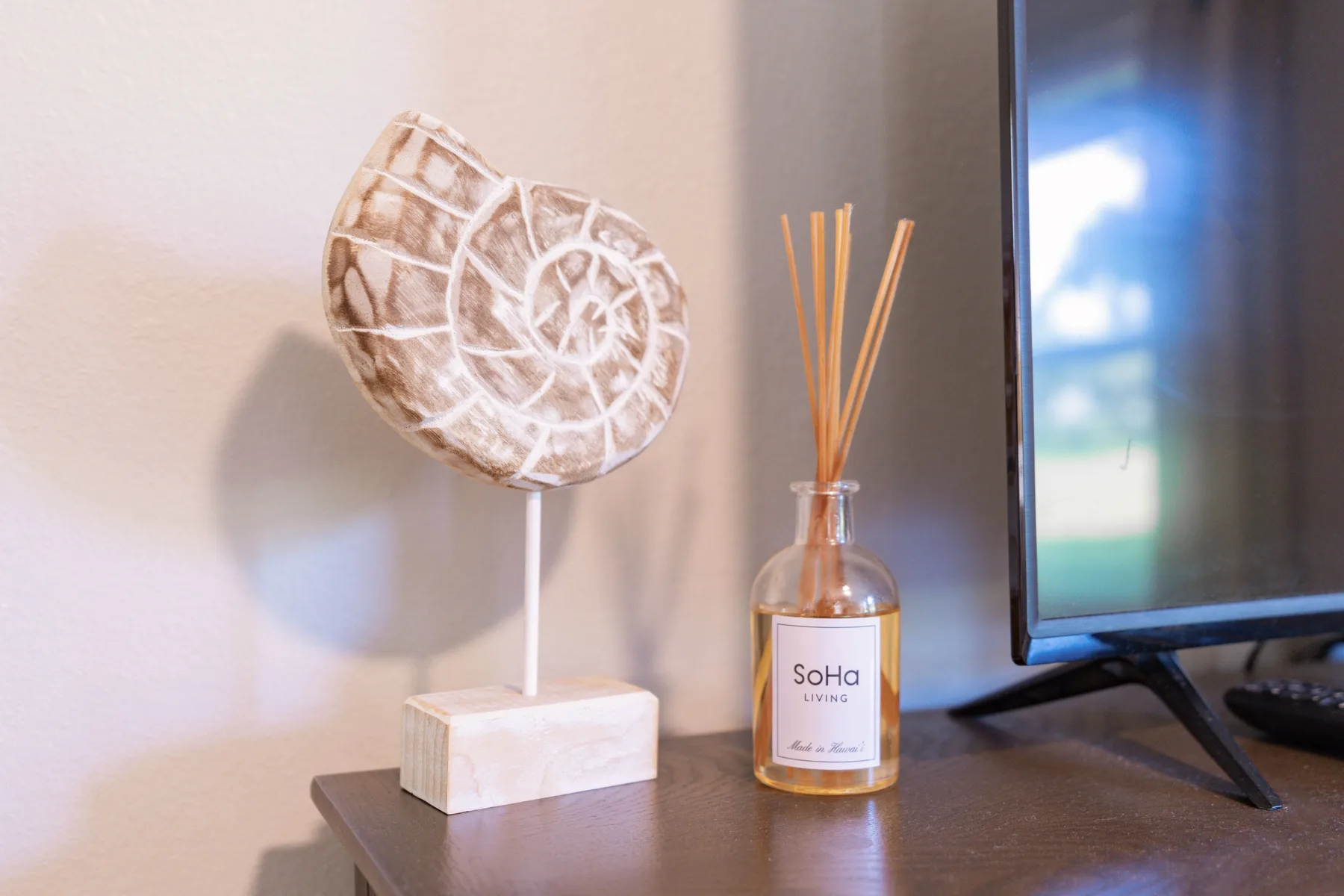 A television and reed diffuser sit on a table beside a decorative shell.