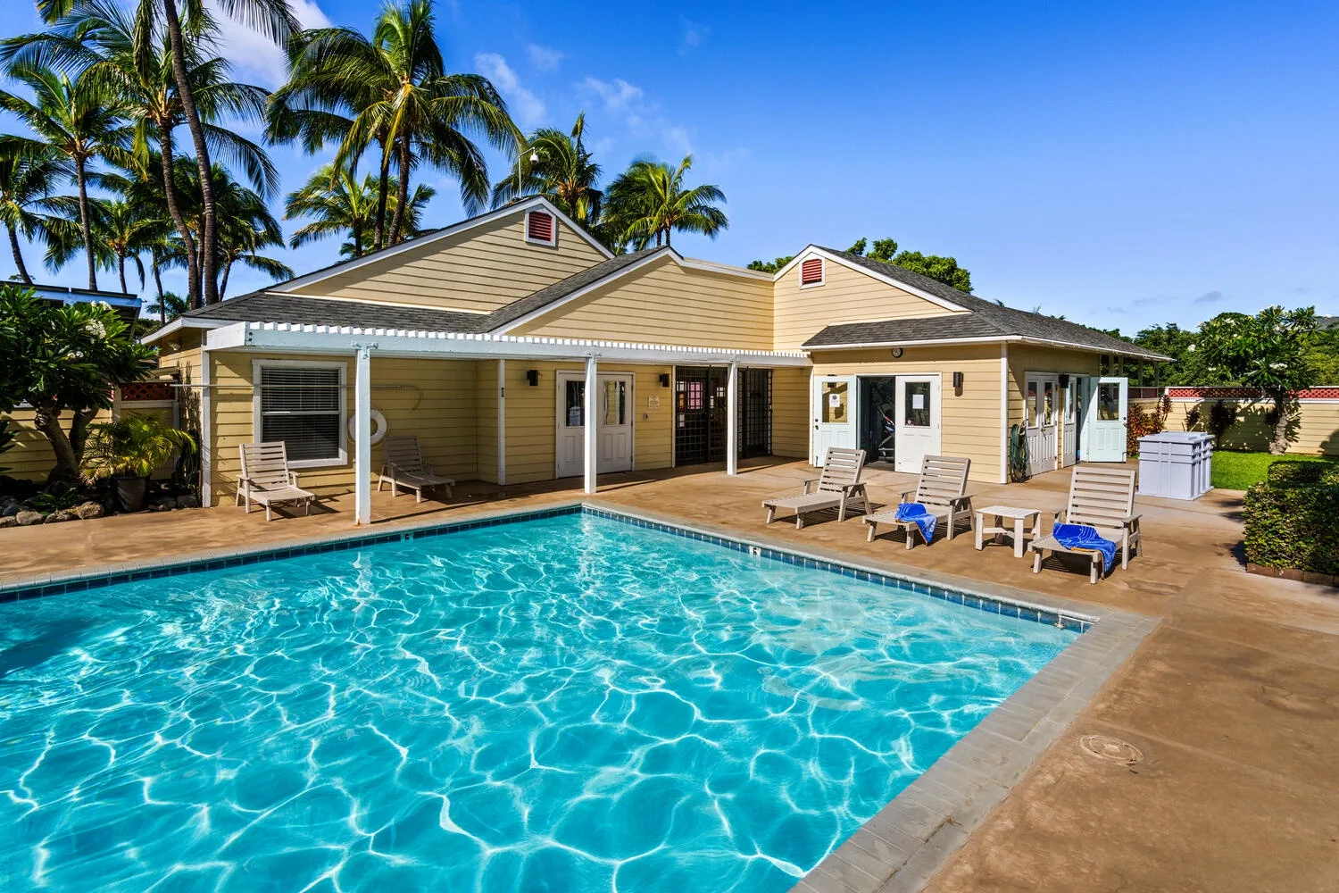 A swimming pool sits beside a single-story house under palm trees.