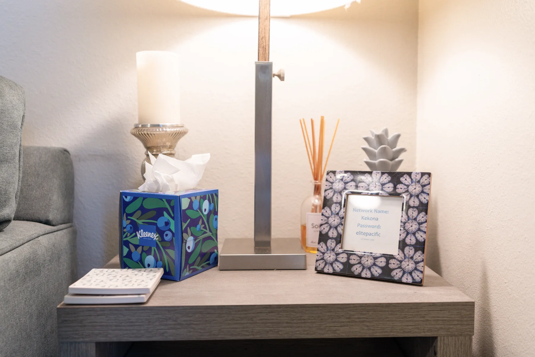 A bedside table holds a tissue box, a framed note, and a lamp.