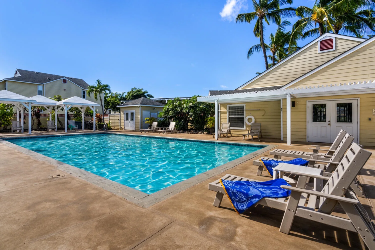 An outdoor swimming pool beside a low building and rows of lounge seating.