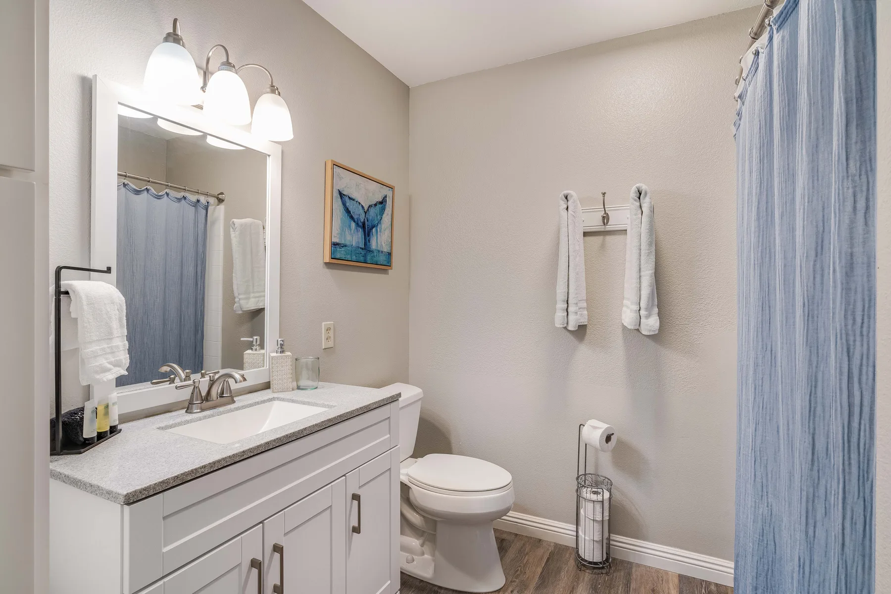 A bathroom with a vanity, toilet, and blue shower curtain.