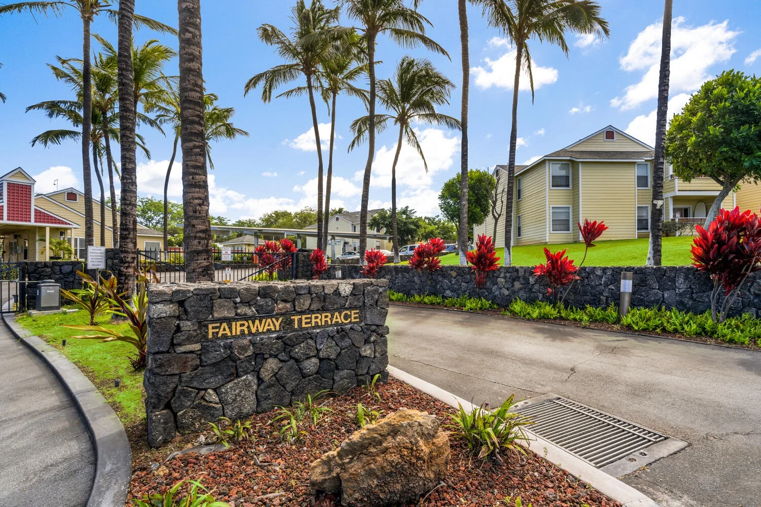 A residential complex with a stone entrance sign and palm trees.