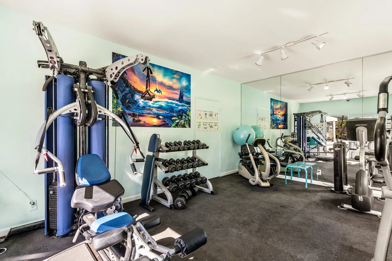 A home gym with exercise machines, dumbbells, and a mirrored wall.