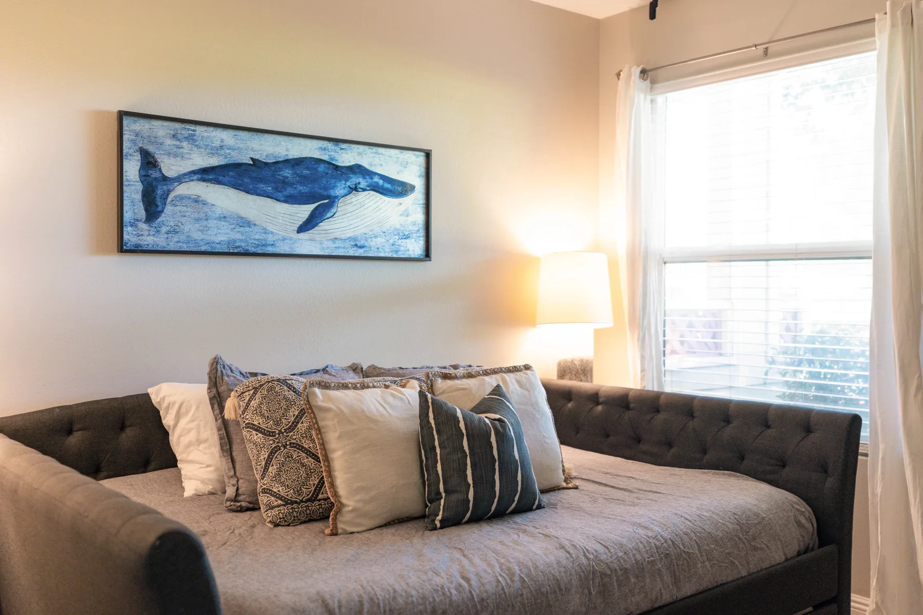 A bedroom with a tufted bed, decorative pillows, and framed whale artwork.