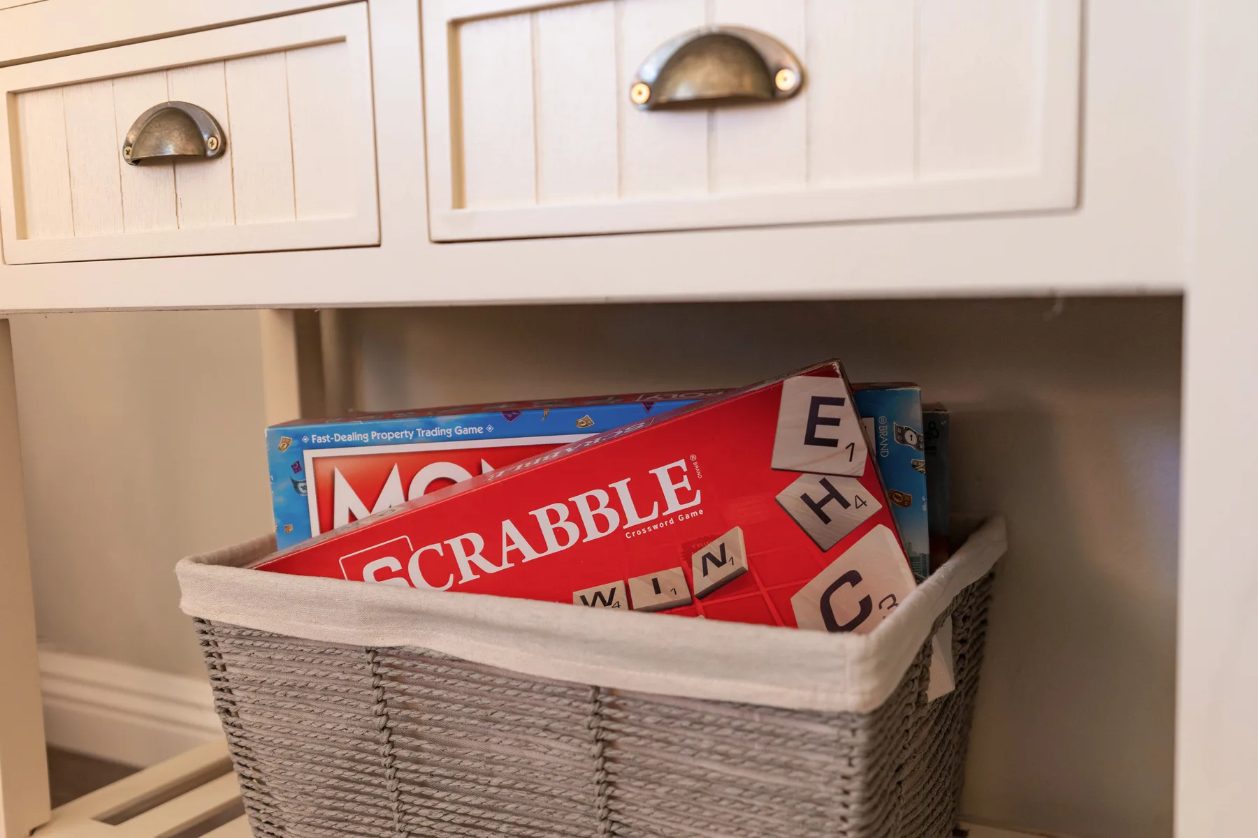A woven basket of board games sits in an open shelf beneath white drawers.