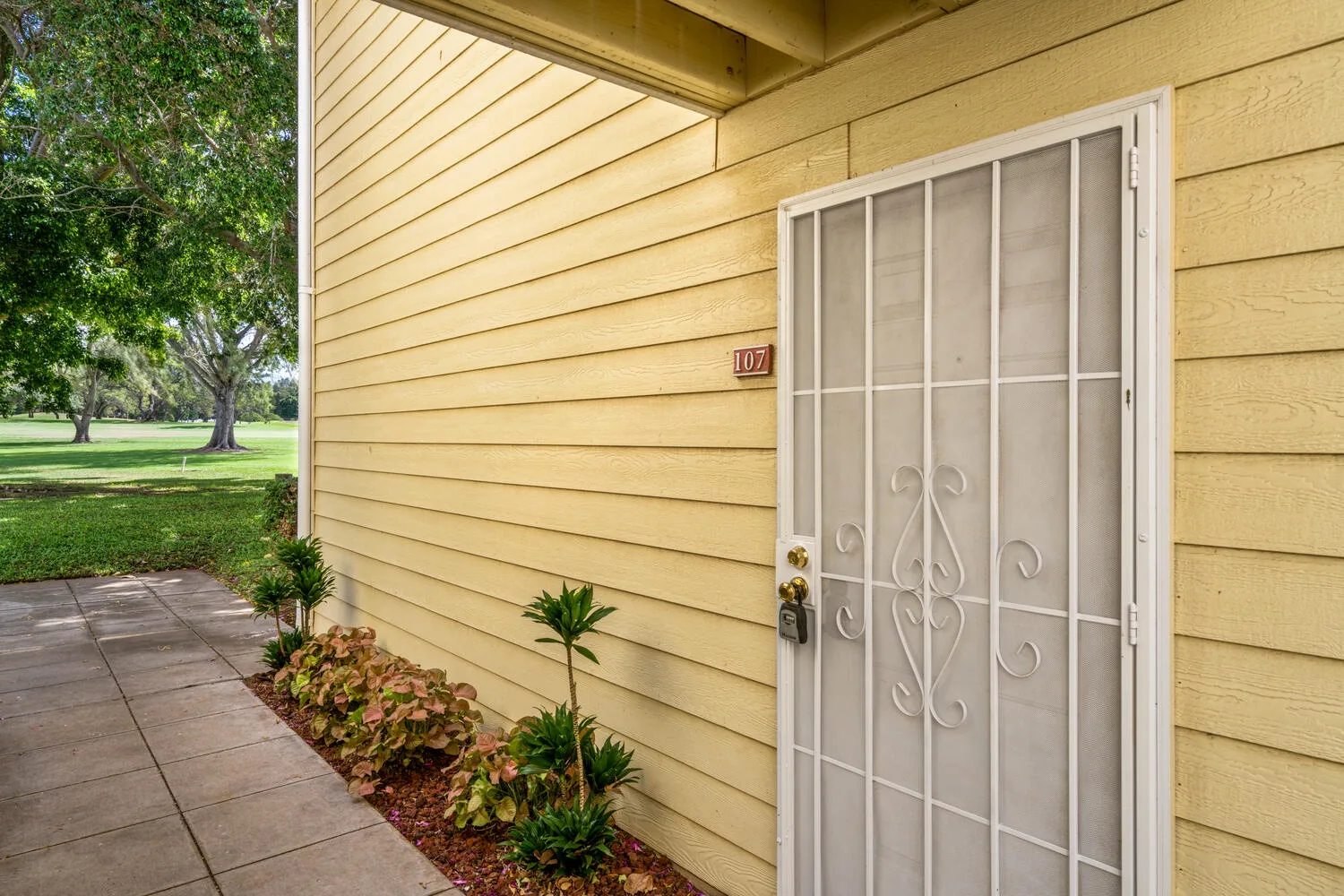A yellow building entrance with a white security door beside a landscaped walkway.