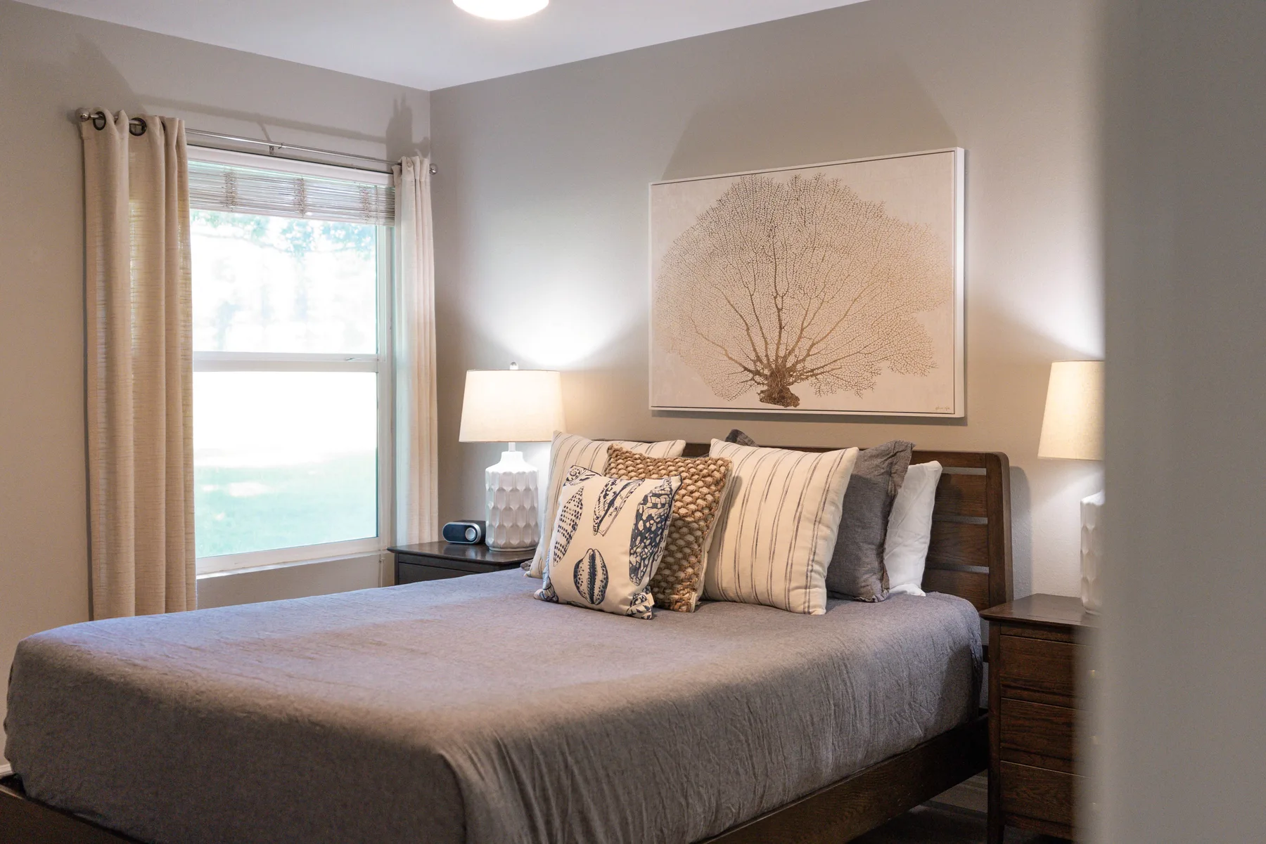 A bedroom with a neatly made bed, bedside lamps, and a large framed print.