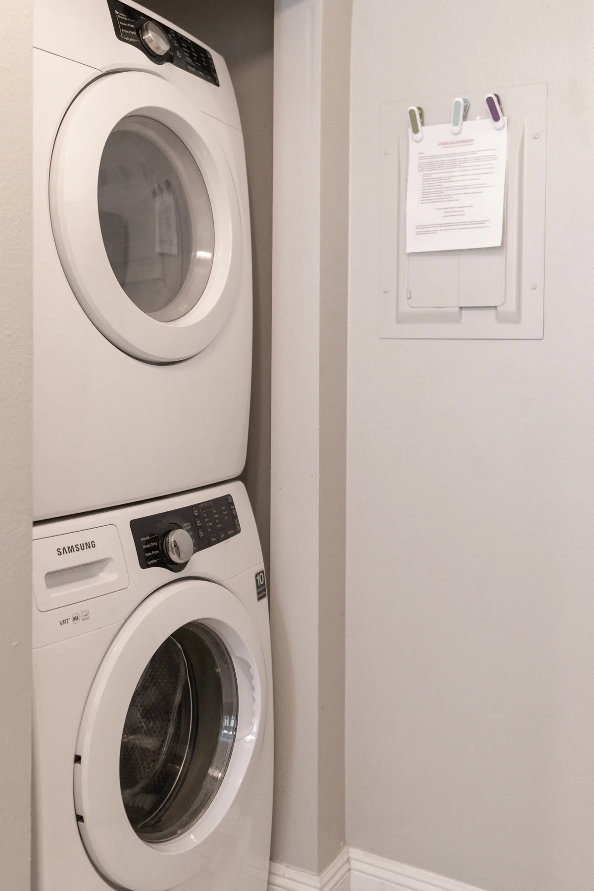 A laundry area with stacked front-loading washing machines beside a posted notice.