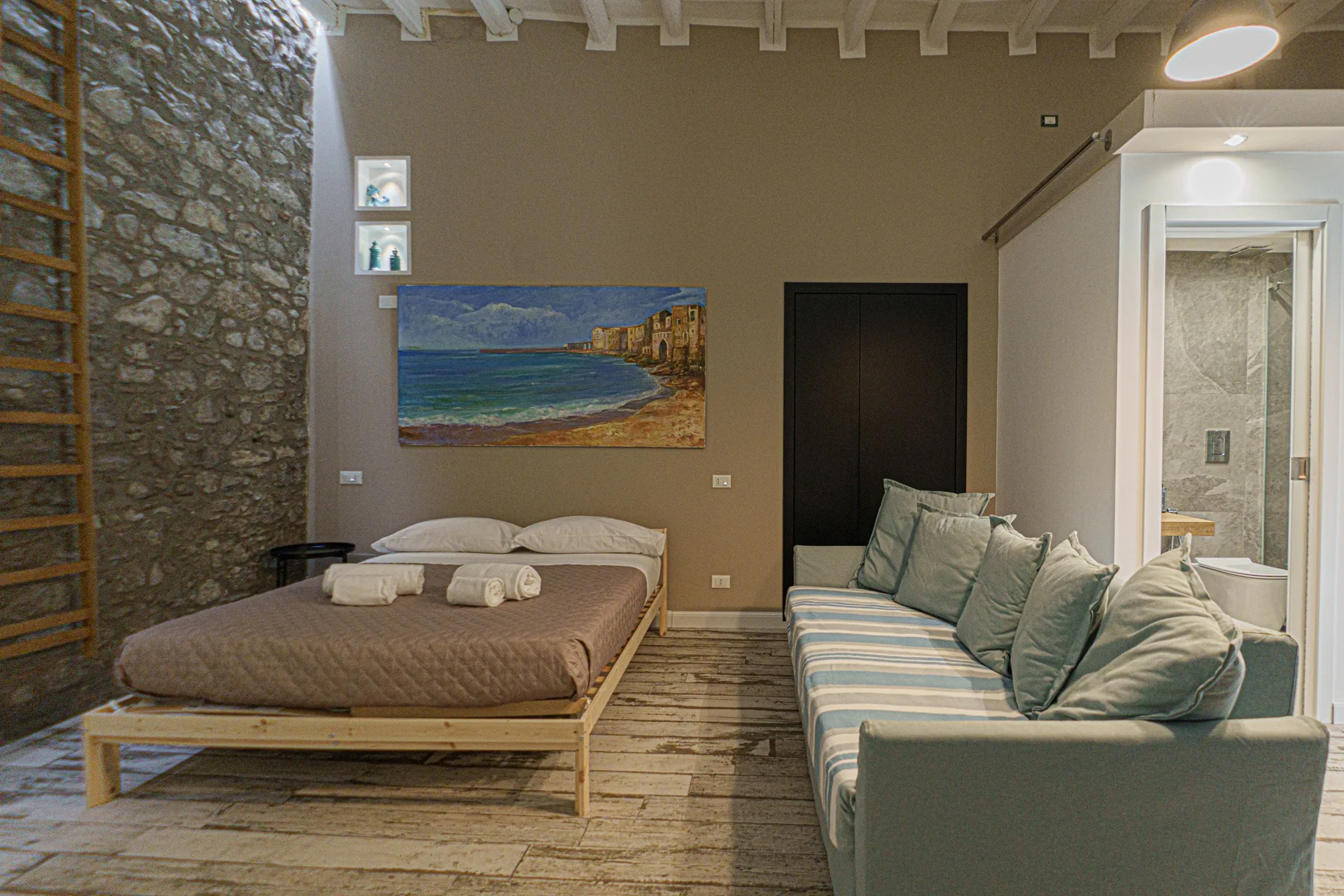 A bedroom with a low bed, a sofa, and a beach painting on the wall.