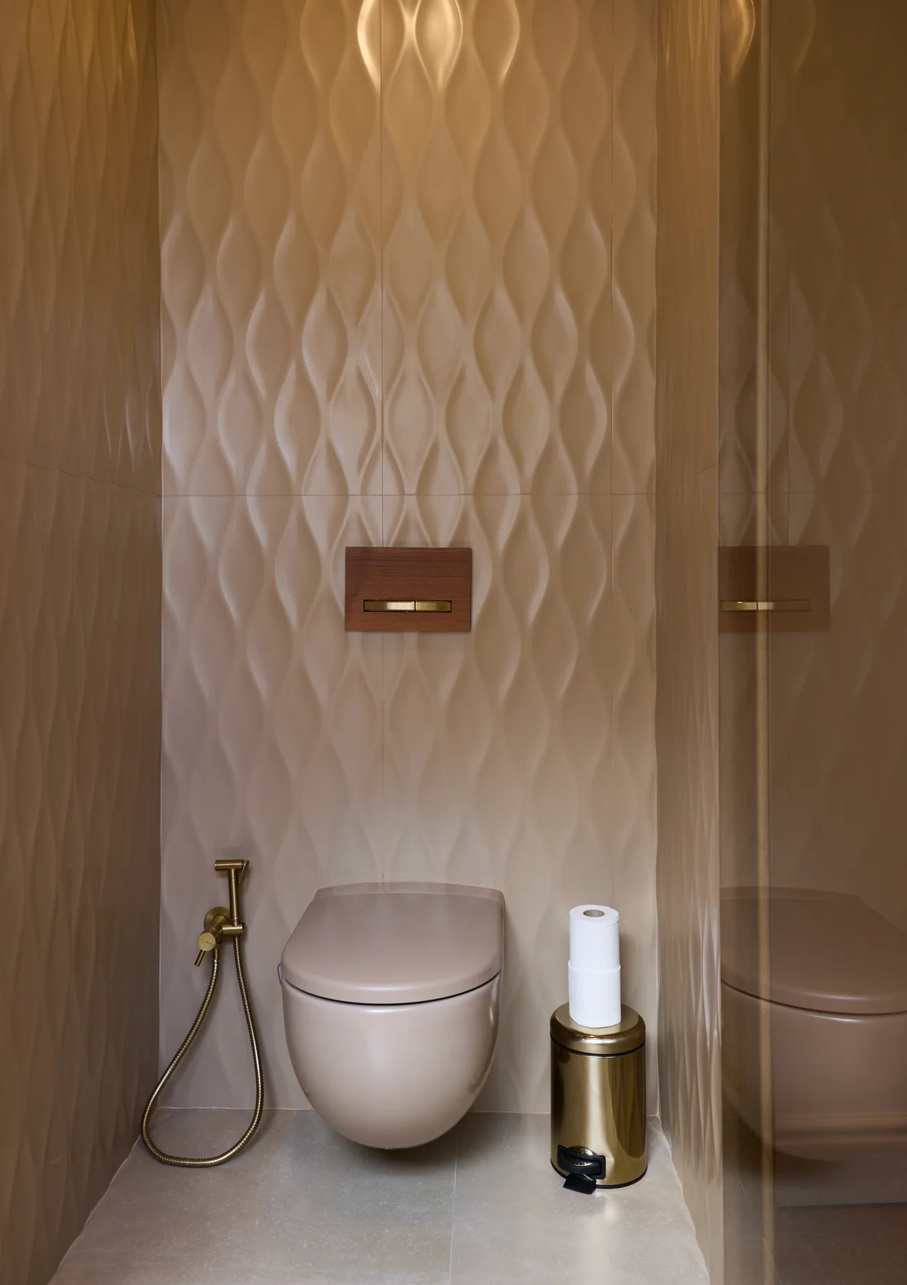 A toilet sits against a textured wall beside a handheld bidet sprayer.