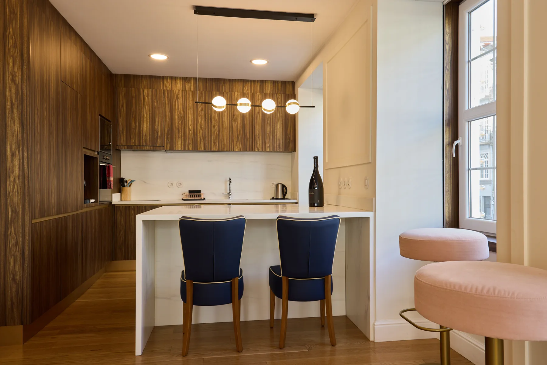 A modern kitchen with a white island and two dark blue seats.