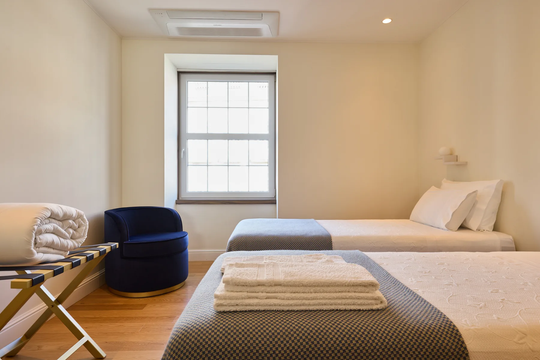 A bedroom with two beds, a window, and a blue chair.