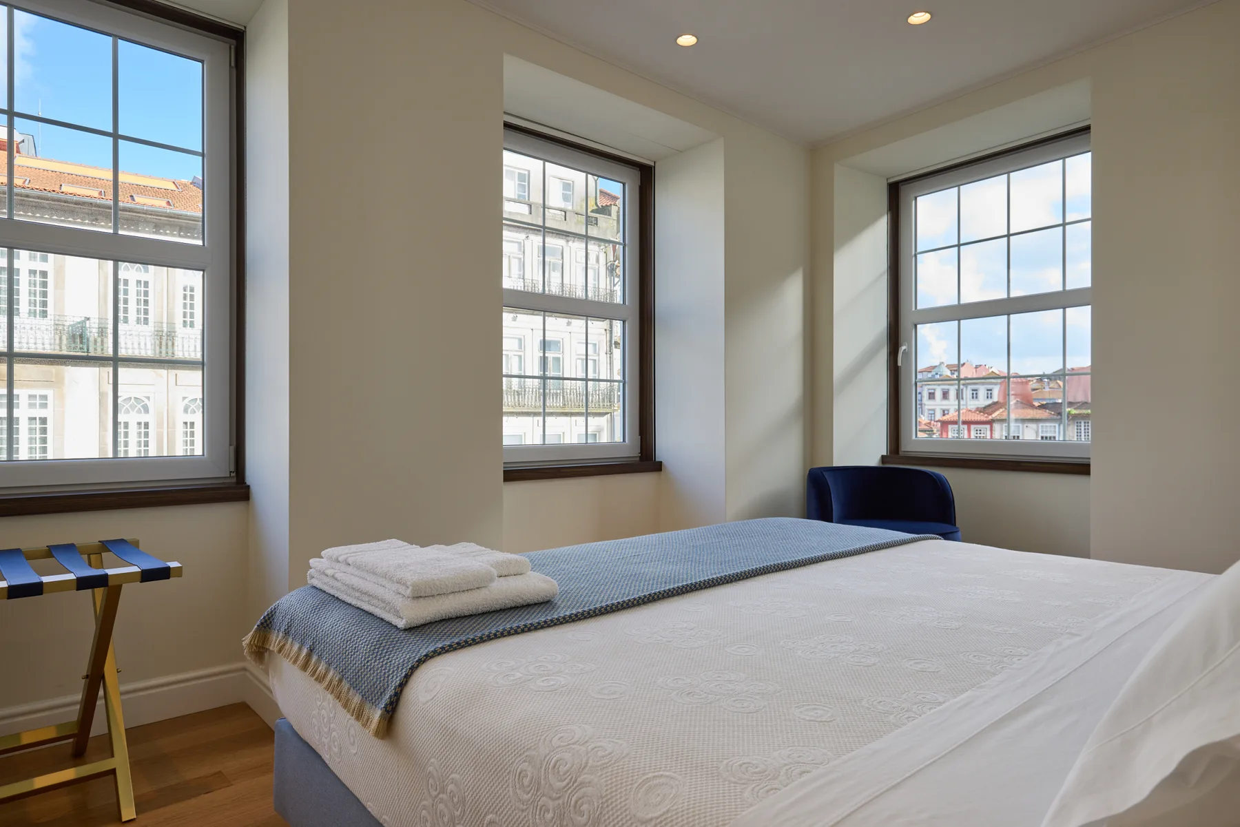 A bright bedroom with a neatly made bed and three large windows.
