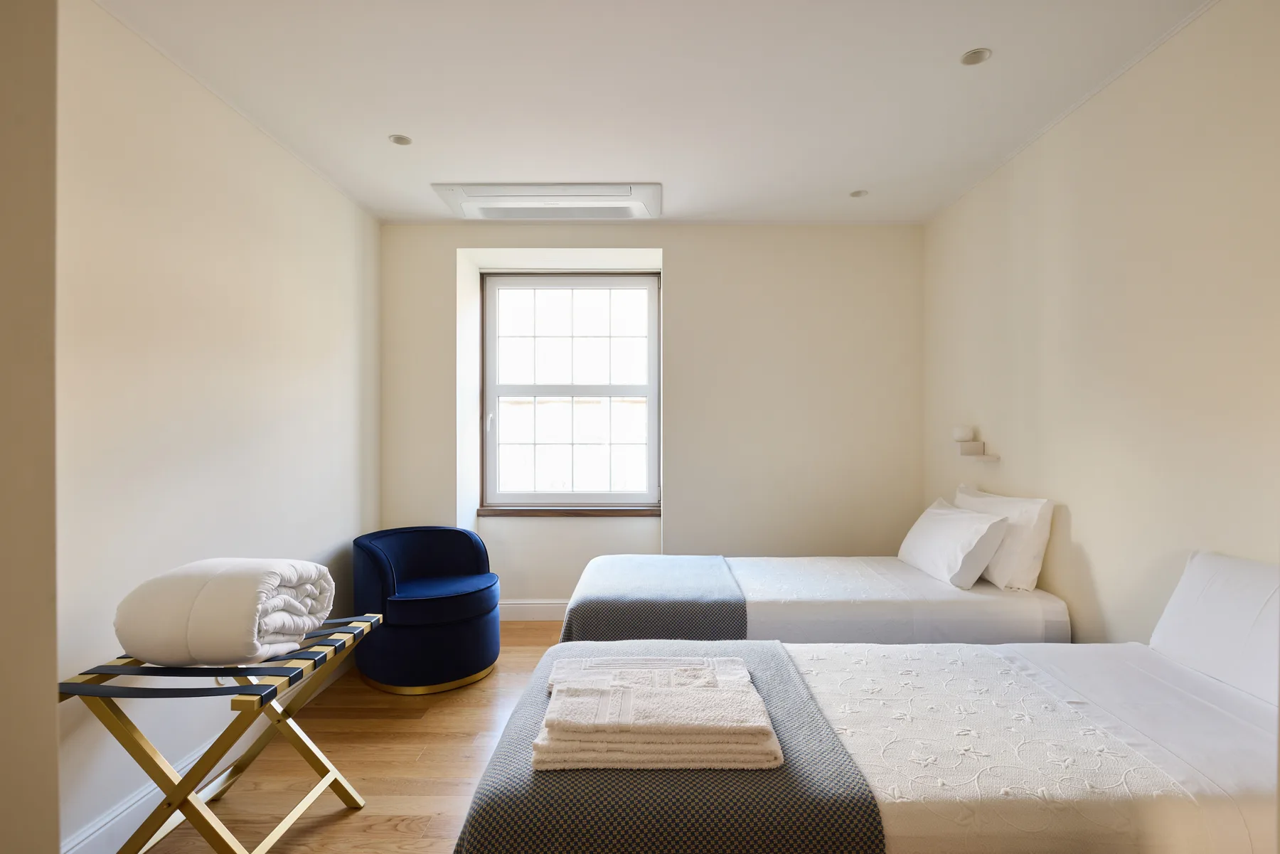 A bedroom with two beds, a window, and a small seating area.