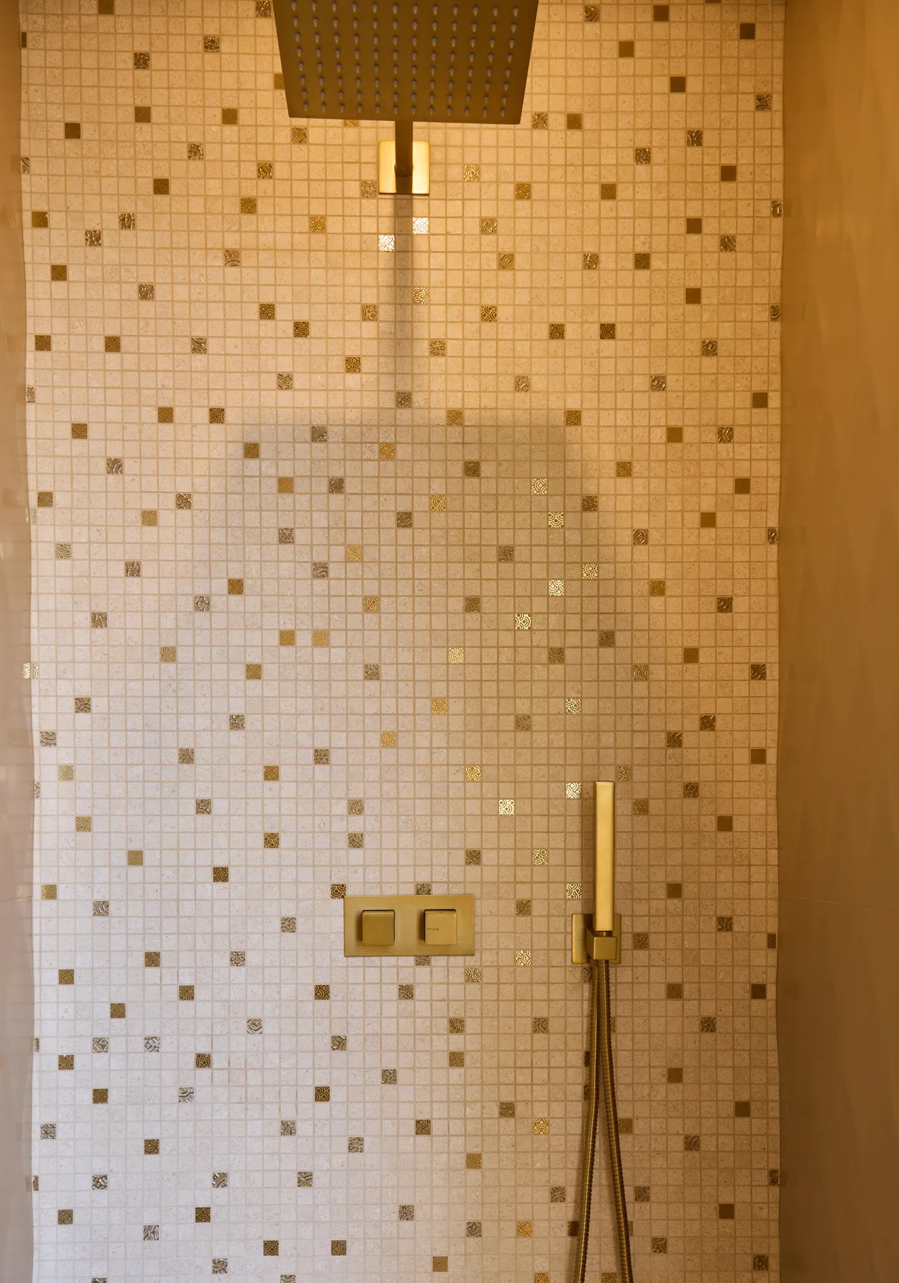 A tiled shower wall with a handheld shower fixture.