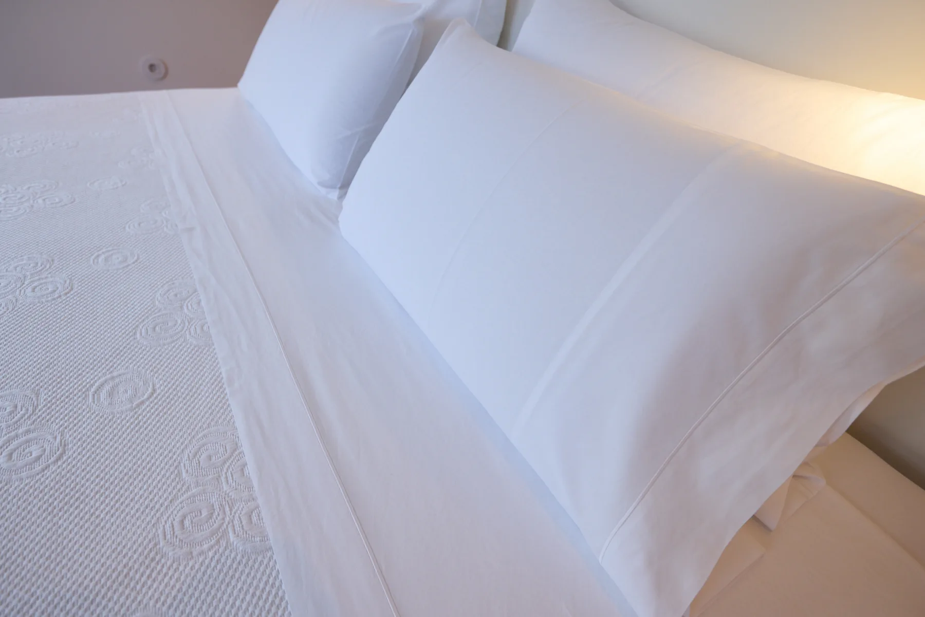 A bed with white linens and pillows in a bedroom.