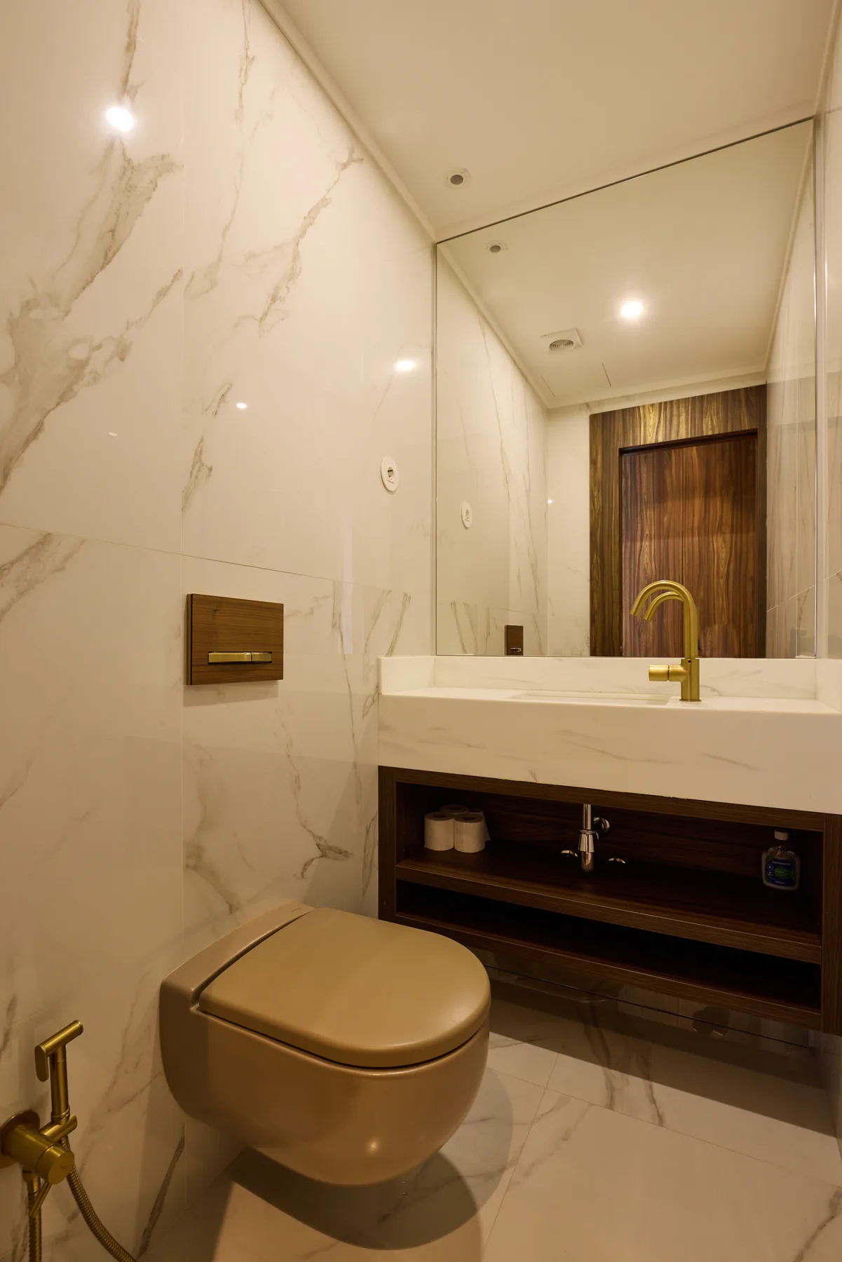 A bathroom with a wall-mounted toilet and a vanity with a gold faucet.