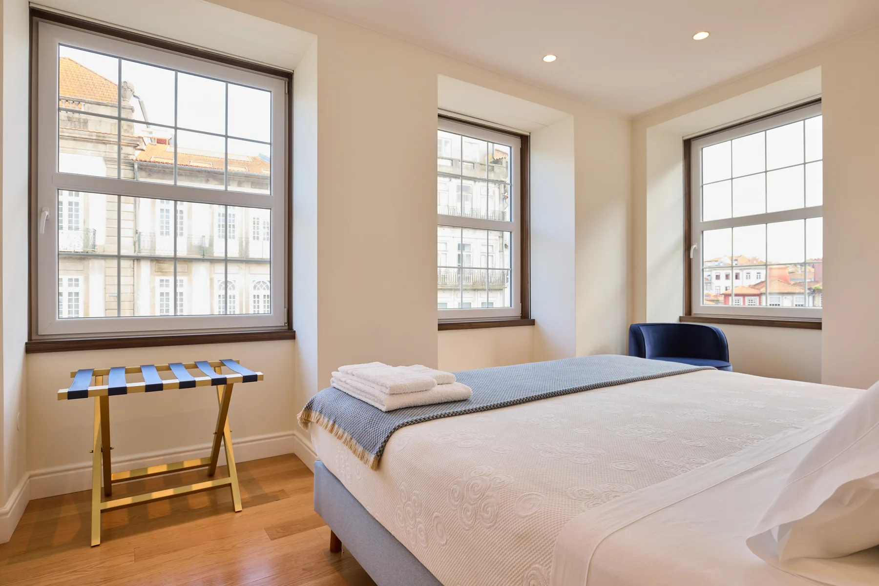 A bedroom with a neatly made bed and three large windows.