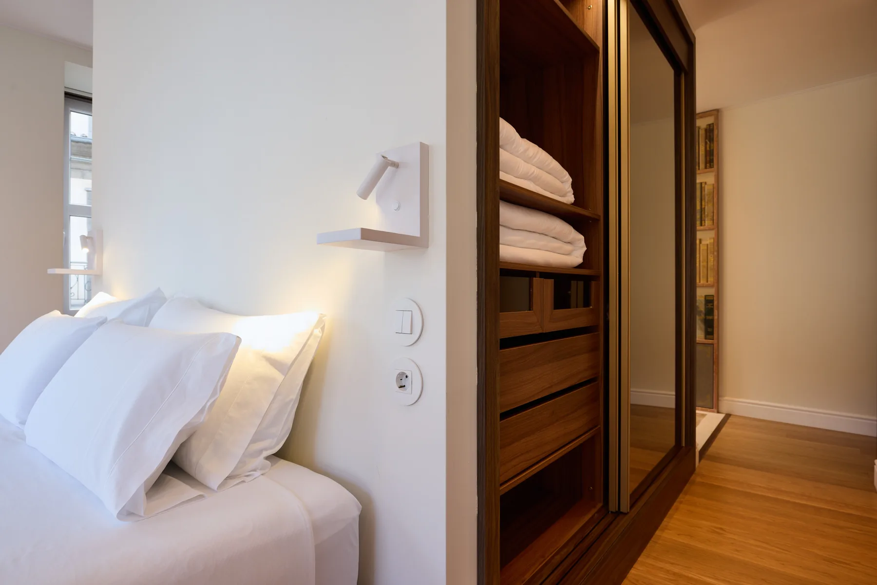 A bedroom with a neatly made bed beside built-in wooden storage.