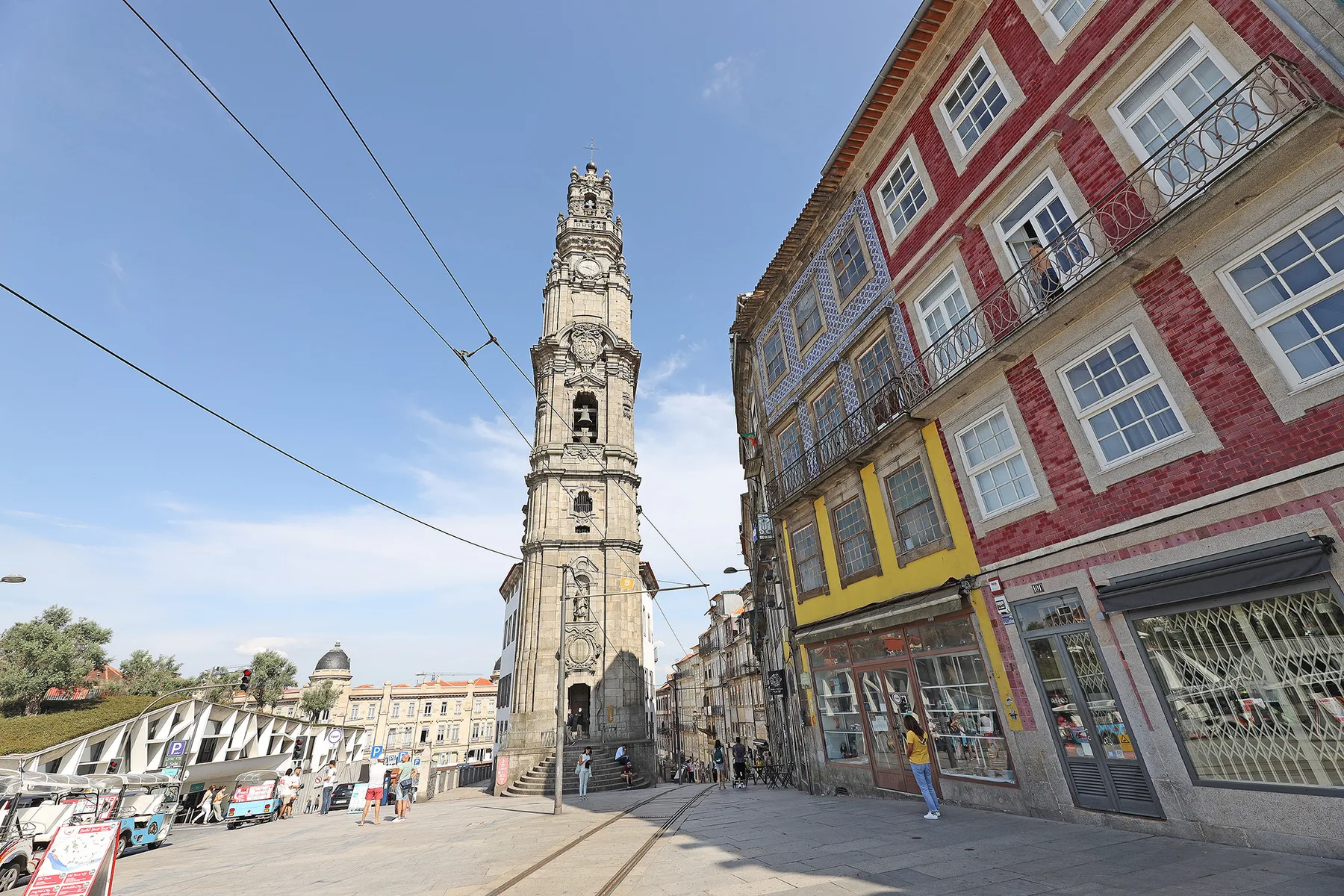 A tall stone tower stands beside colorful buildings in a sunlit city square.