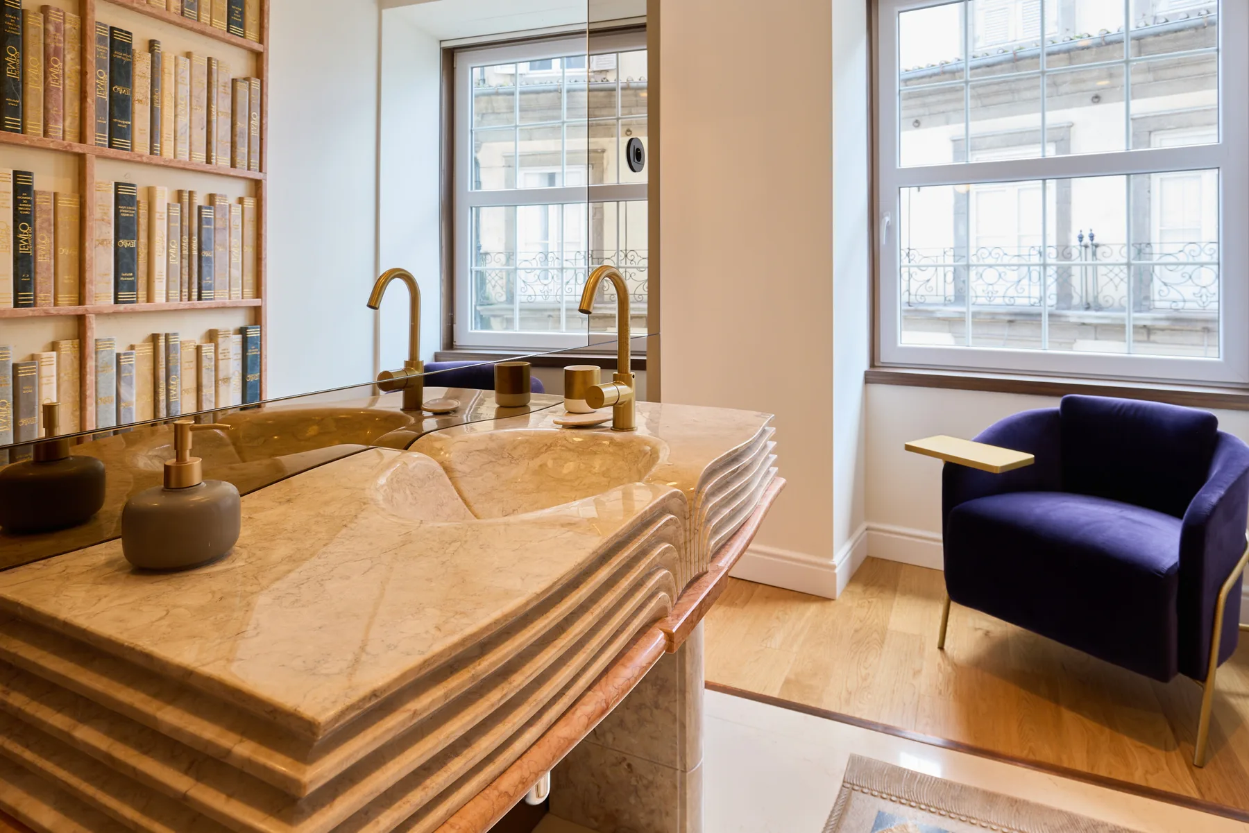 A bright room has a marble counter, bookshelves, and a blue armchair by the windows.
