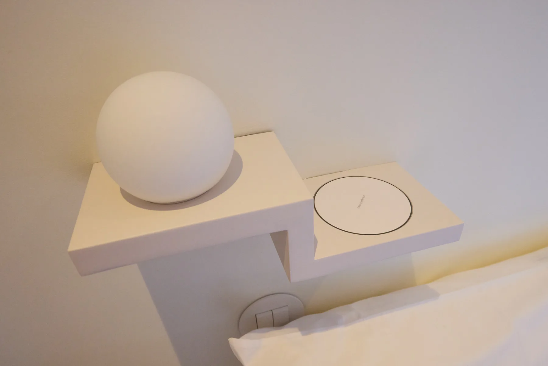 A bedside table holds a spherical lamp beside a circular control panel.