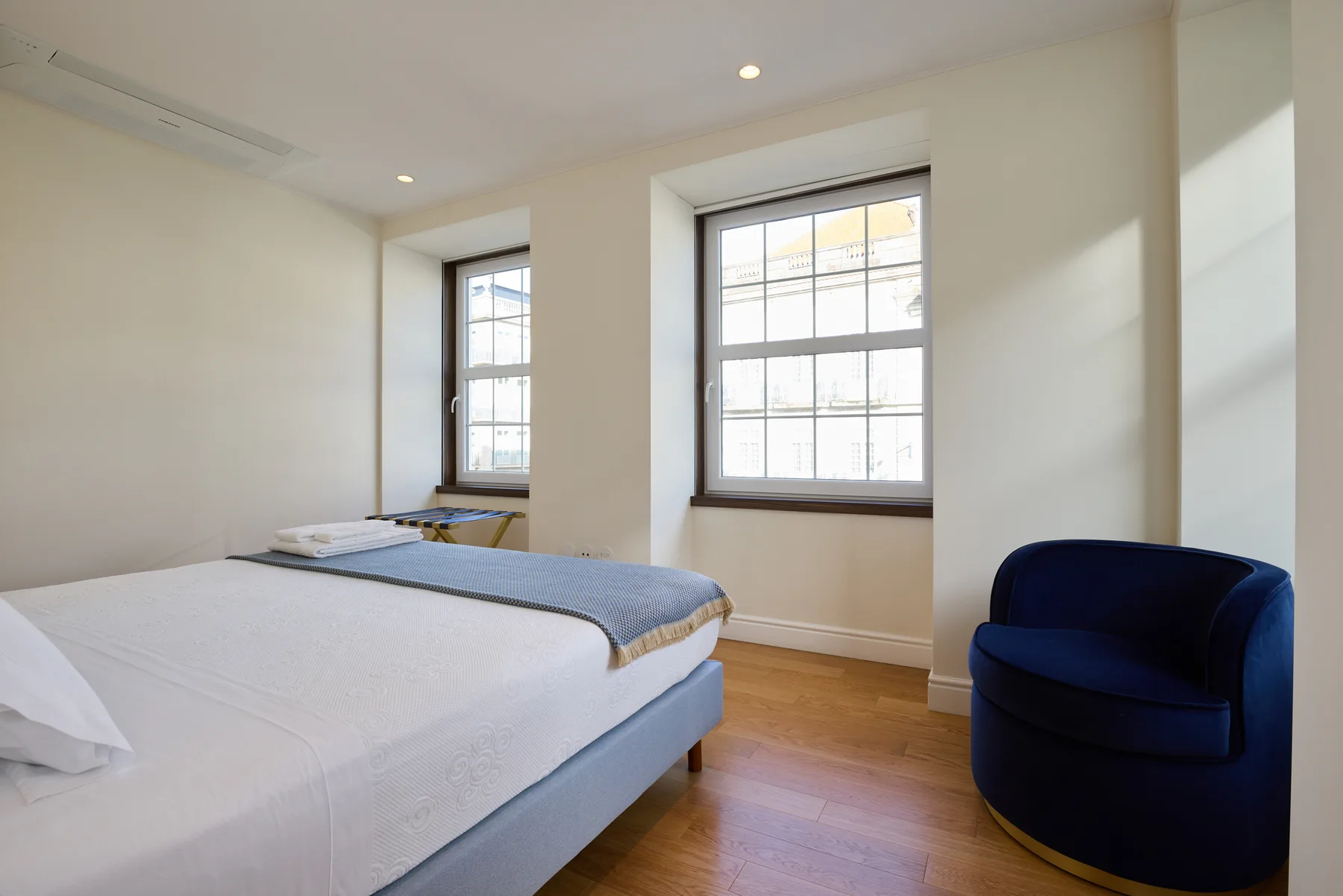 A bedroom with a bed and a blue armchair beside the windows.