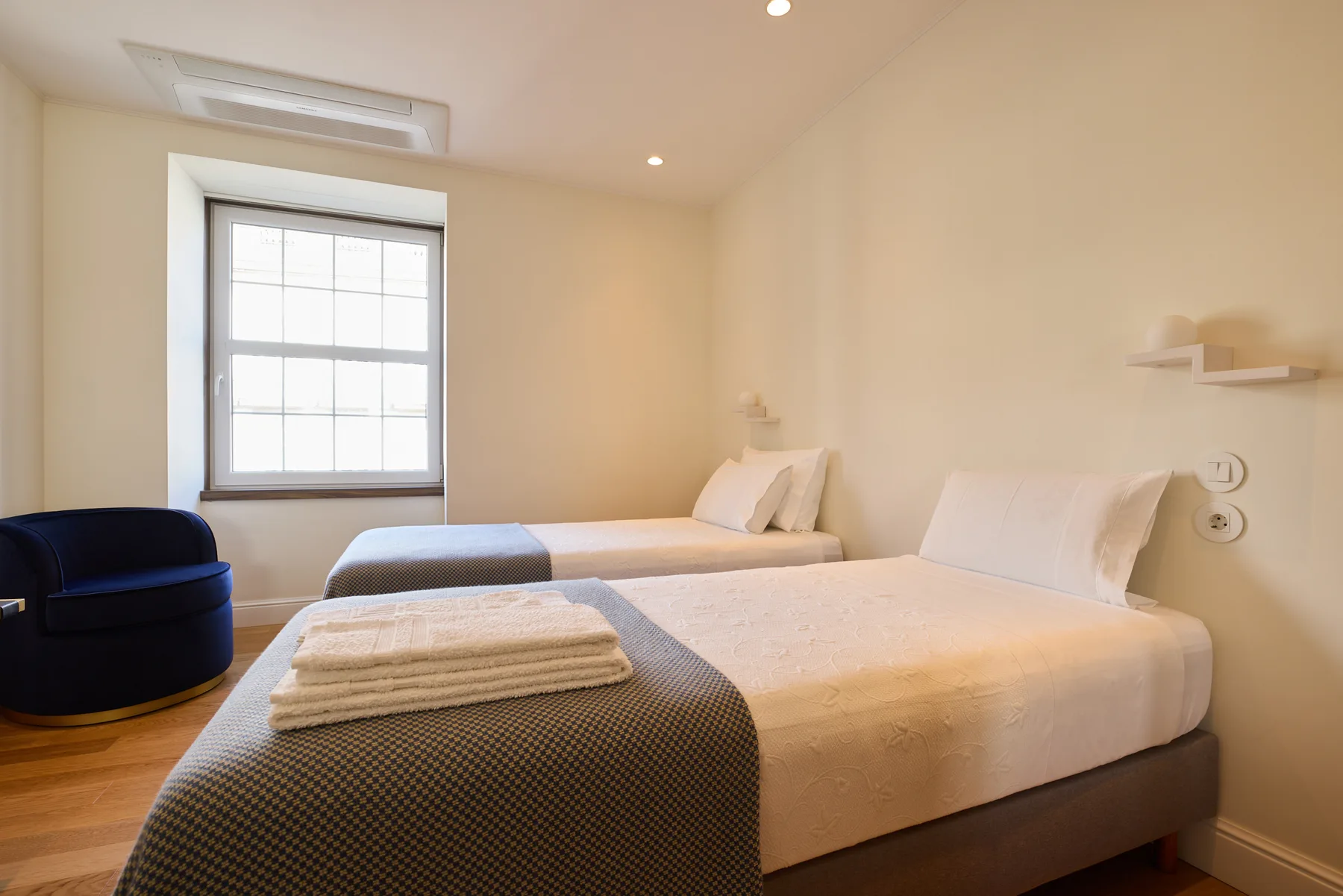 A bedroom with two beds, folded towels, and a window.