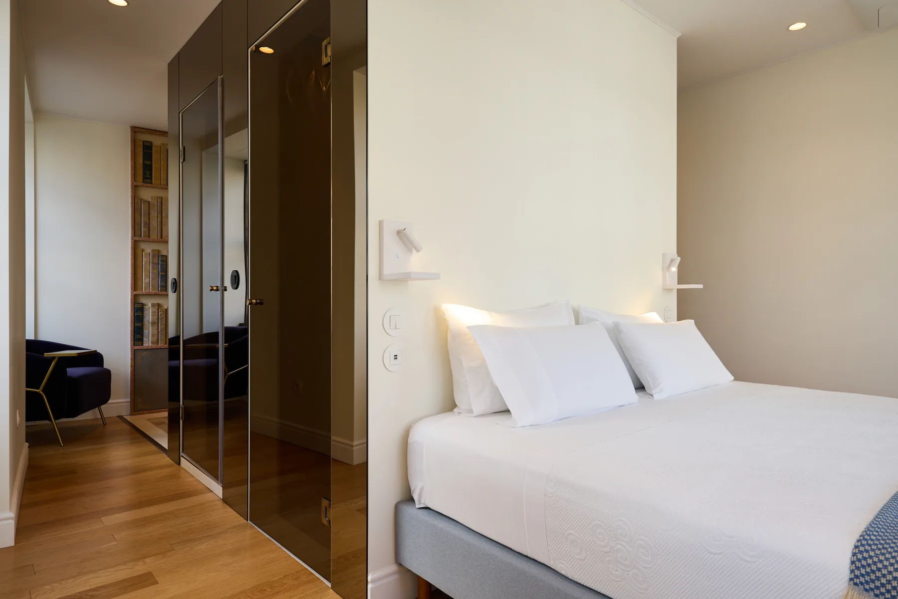 A bright bedroom with a neatly made bed beside mirrored wardrobe doors.