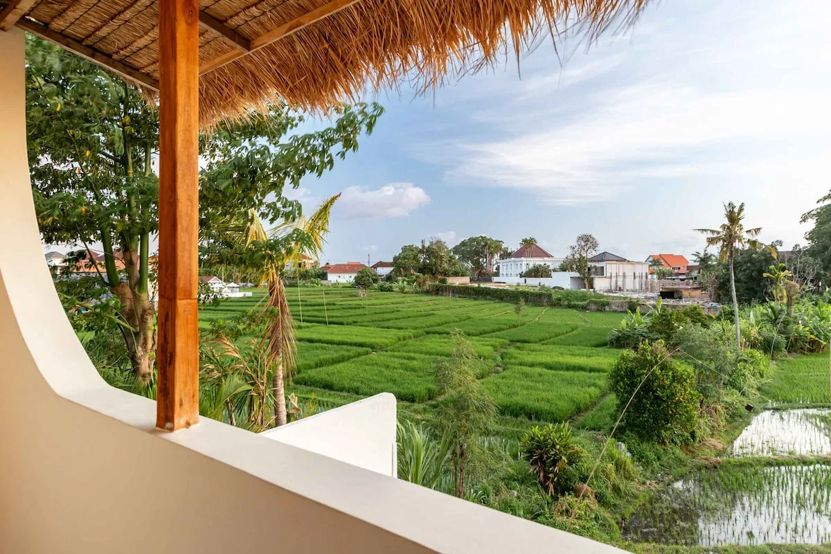 A covered balcony overlooks green fields and scattered buildings.