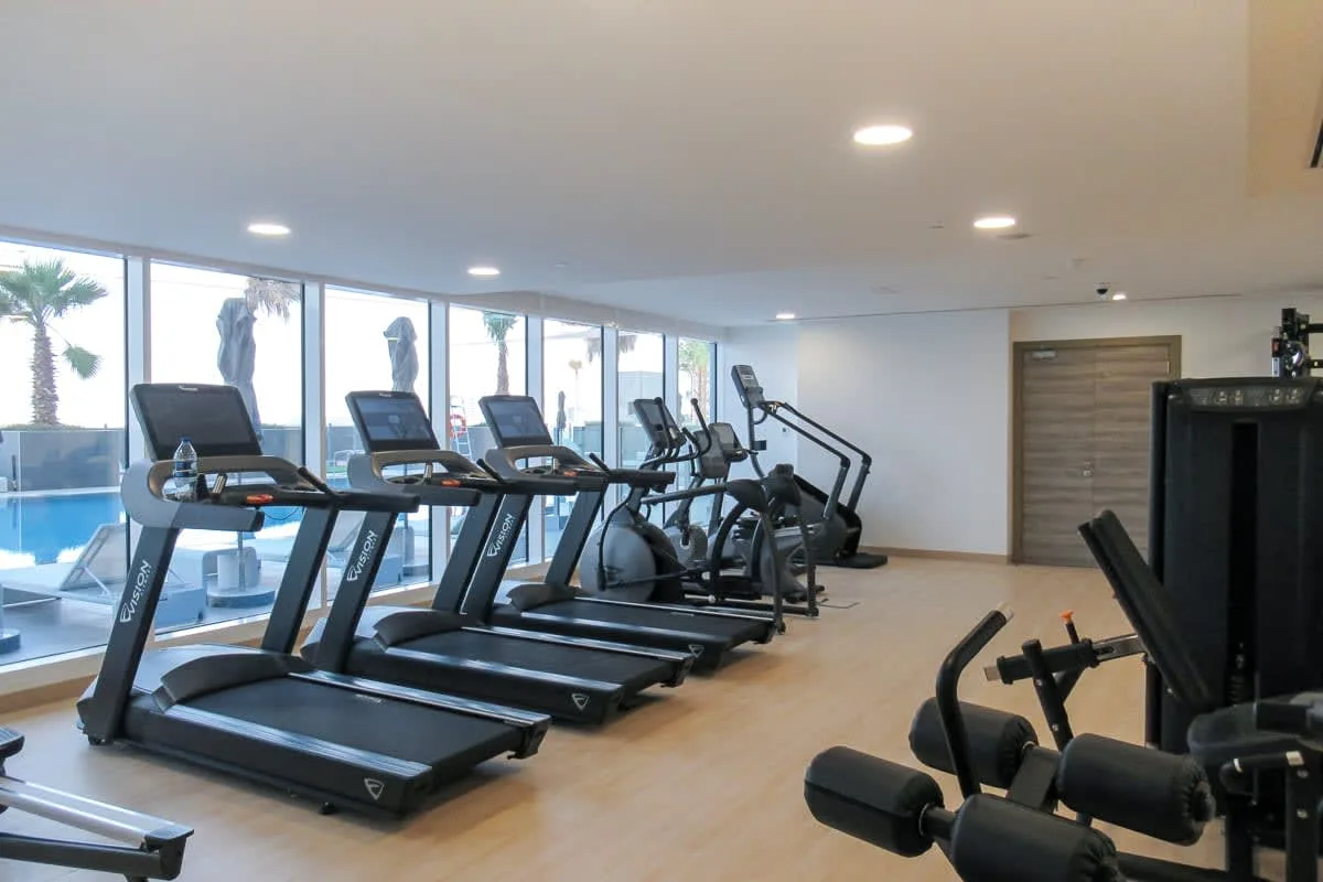 A gym with treadmills and other exercise equipment beside large windows.