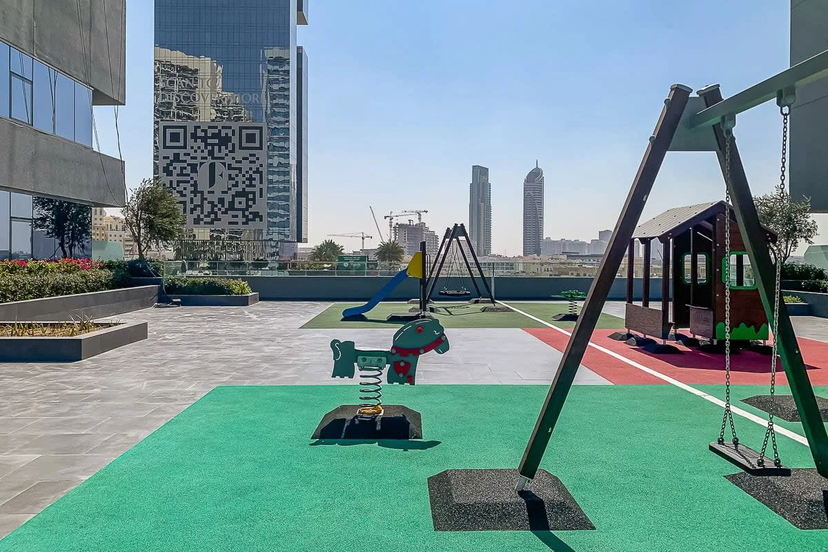 An outdoor playground with swings and spring riders on colorful safety flooring.