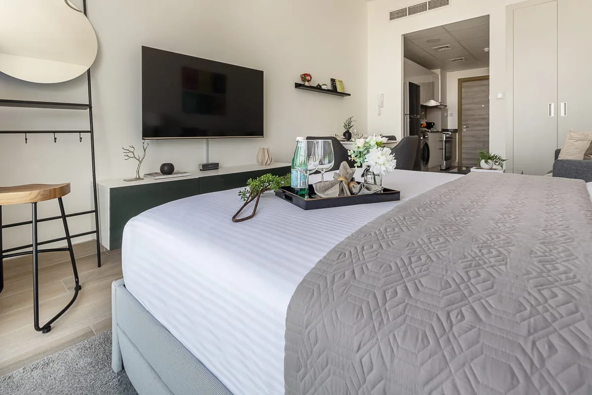A bedroom with a neatly made bed, television, and open doorway.