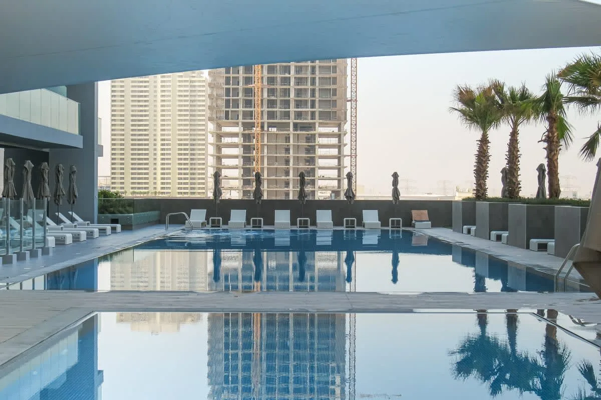 An outdoor swimming pool is surrounded by seating and palm trees.