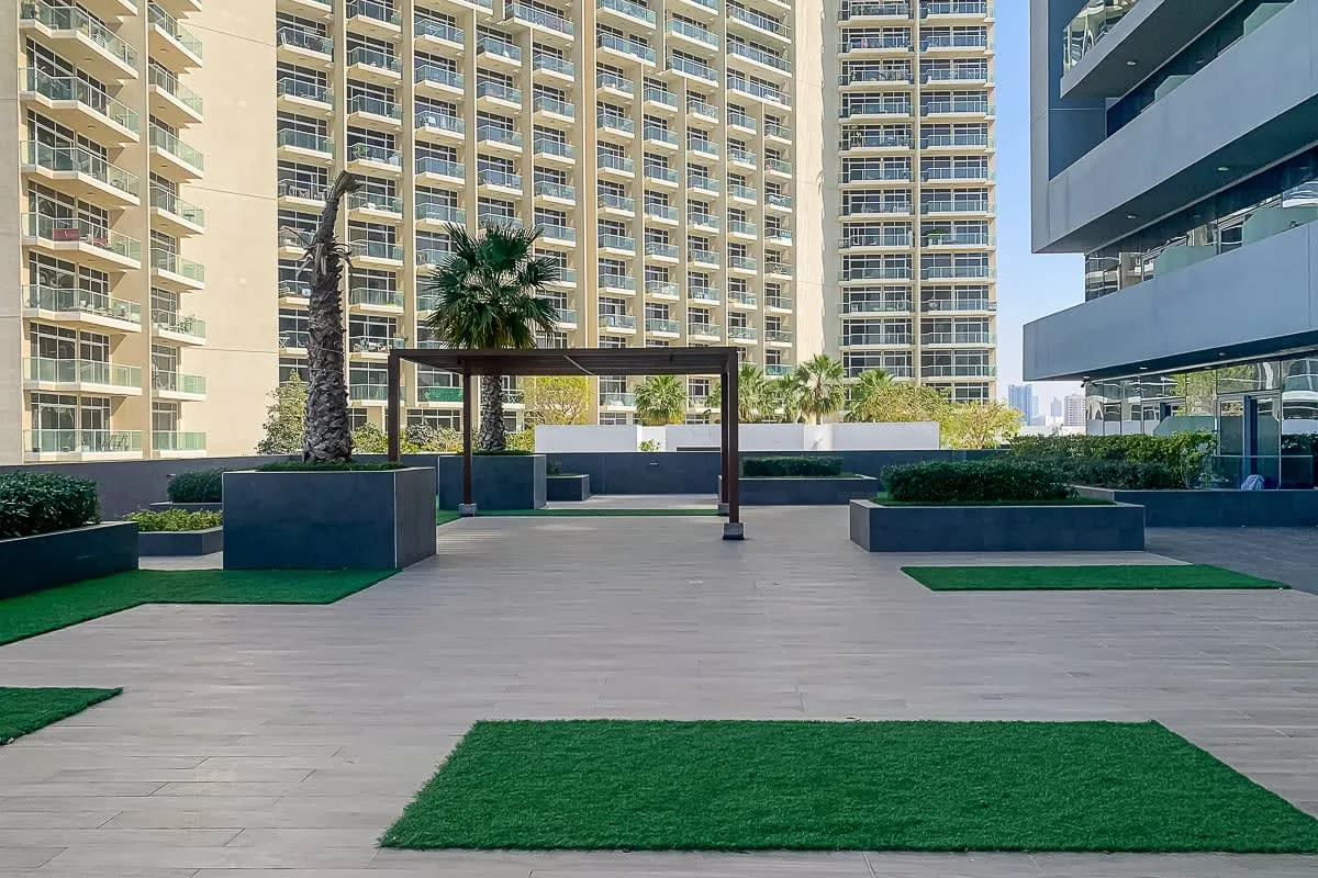 An outdoor courtyard with paved walkways, planted areas, and surrounding high-rise buildings.