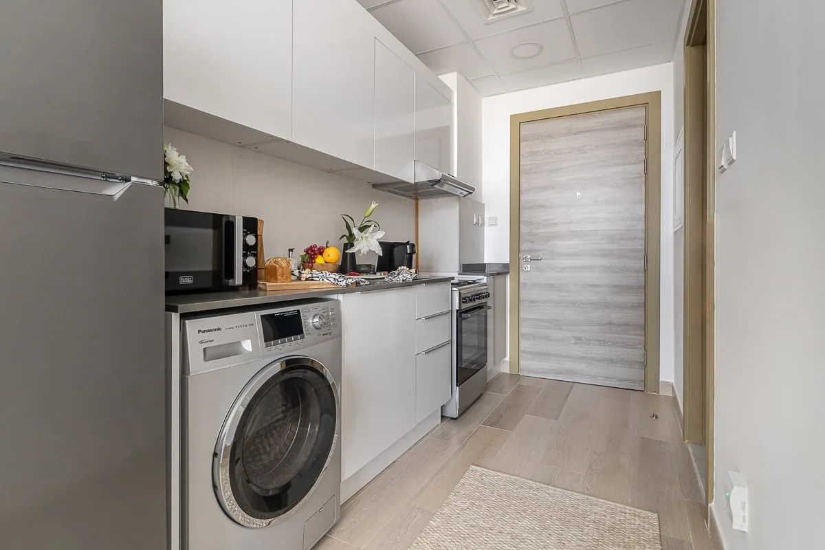 A compact kitchen with white cabinetry, countertop appliances, and a washing machine.