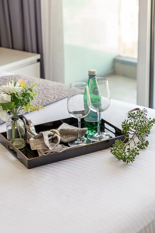 A bedroom with a bed, a tray of glasses, and a bottle of water.