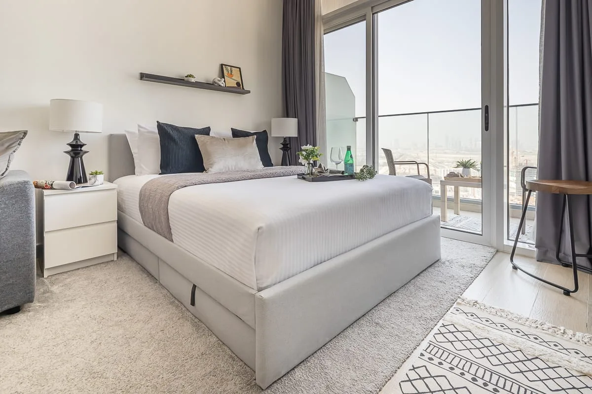 A bright bedroom with a neatly made bed beside large glass doors.