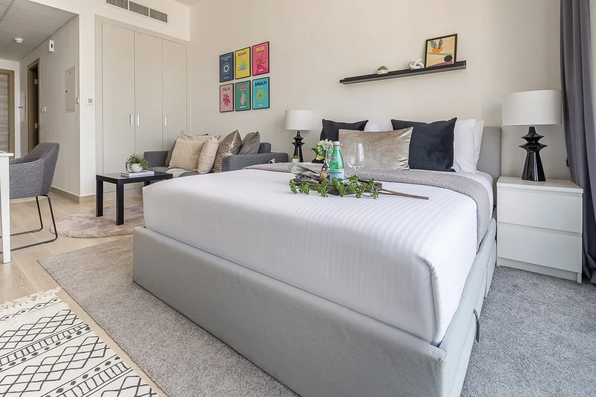 A bright bedroom with a large bed, bedside tables, and a small seating area.