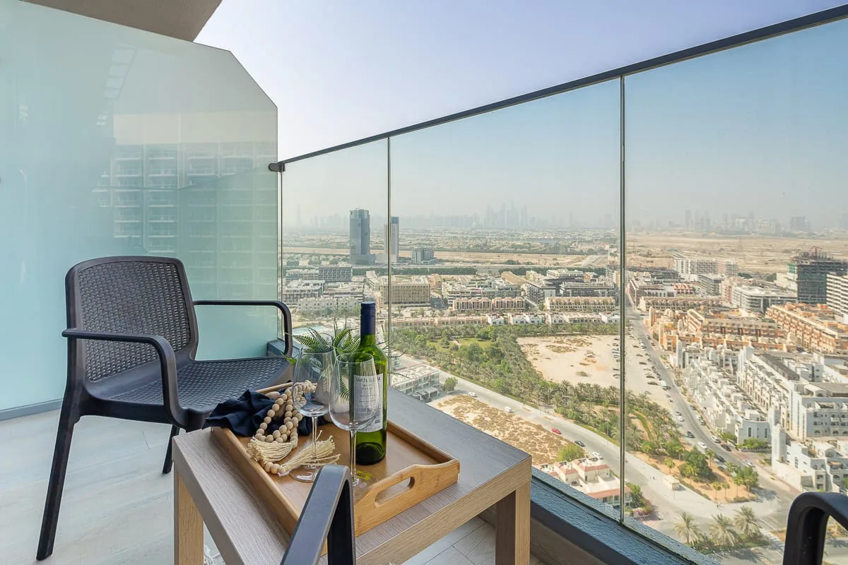 A balcony seating area overlooks the surrounding city through a glass railing.