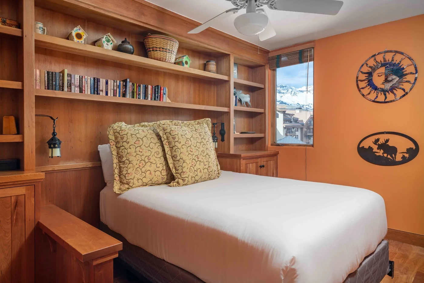 Un dormitorio con una cama, estantes de madera empotrados y una pared naranja.