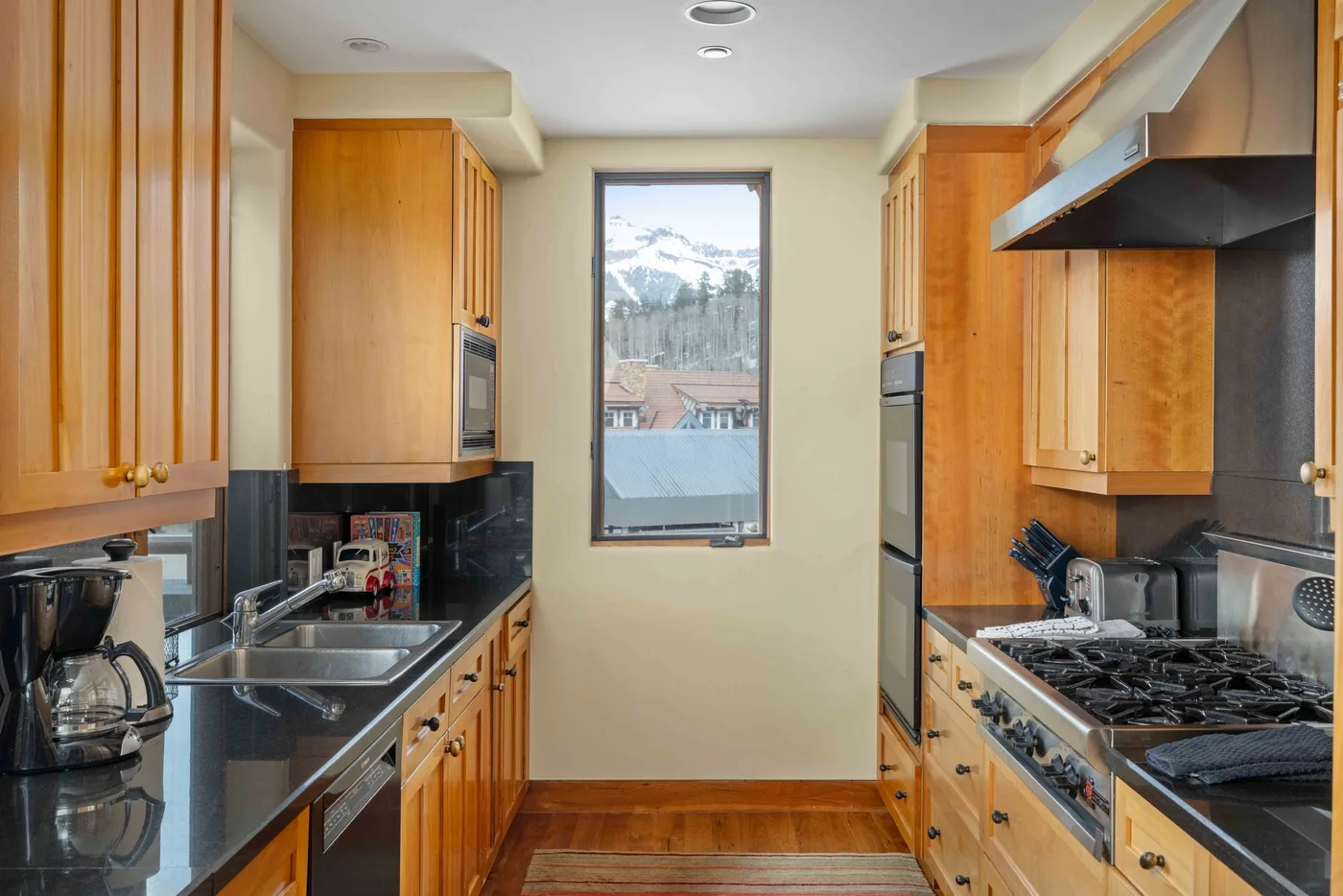 Una cocina estrecha con gabinetes de madera, electrodomésticos de acero inoxidable y una ventana con vistas a las montañas.