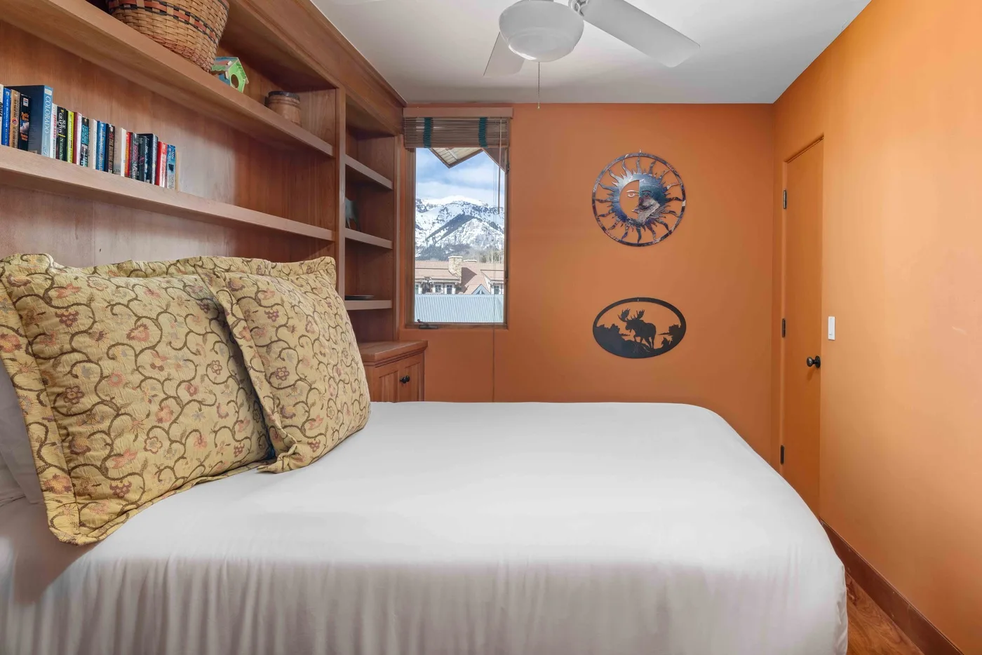Un dormitorio con una cama blanca, almohadas estampadas y estantes de madera empotrados.