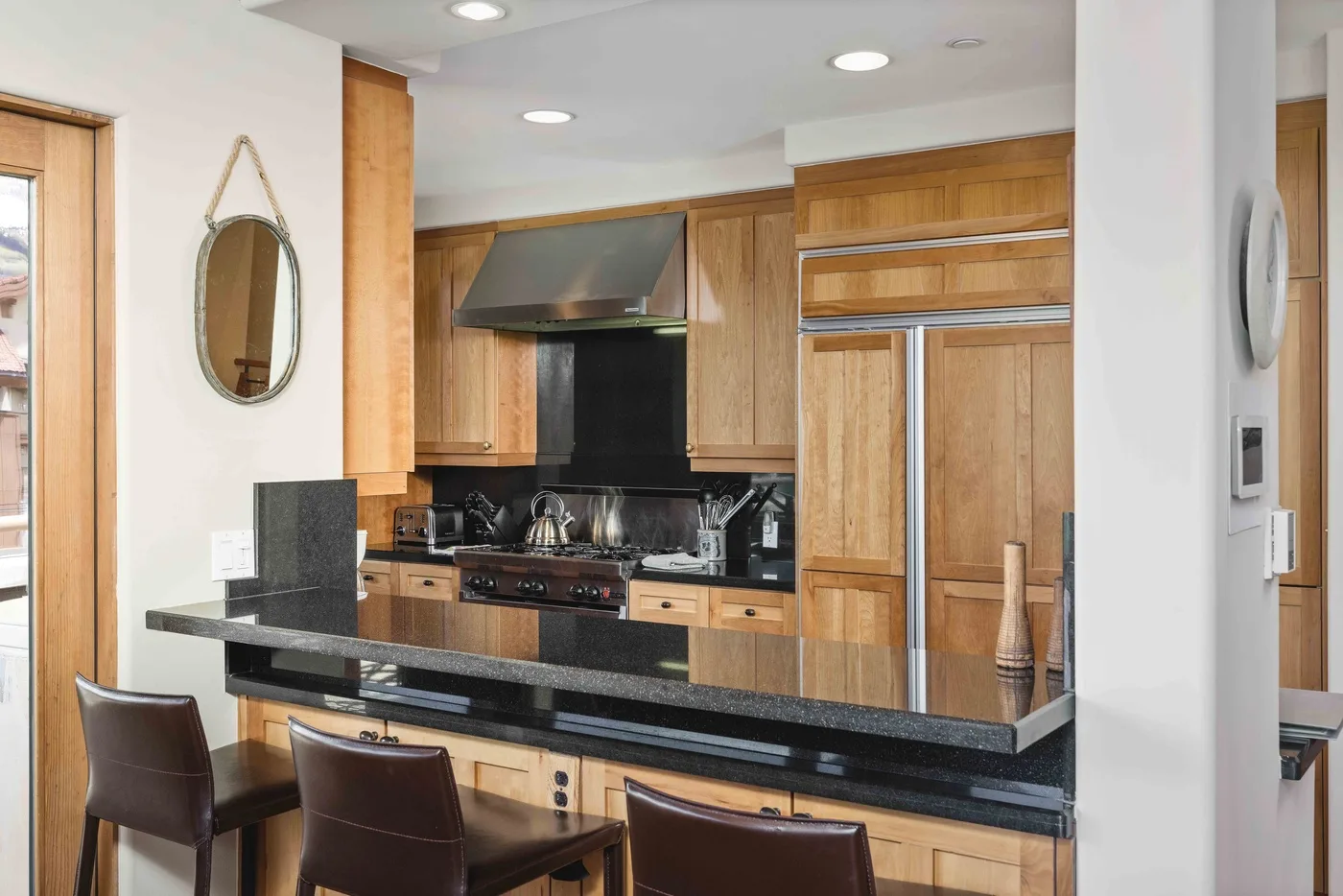 Una cocina con gabinetes de madera, una encimera negra y asientos de barra.