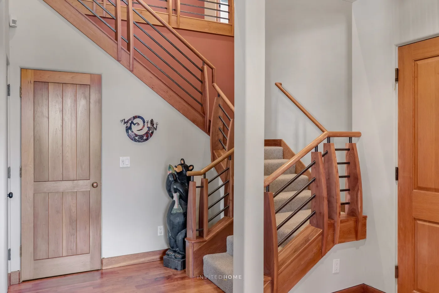 Una escalera residencial con barandillas de madera, un rellano y puertas cercanas.