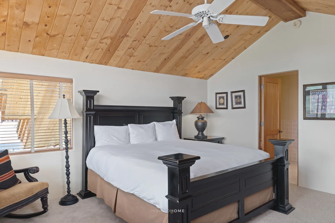 Dormitorio con una cama grande bajo un techo de madera y un ventilador.