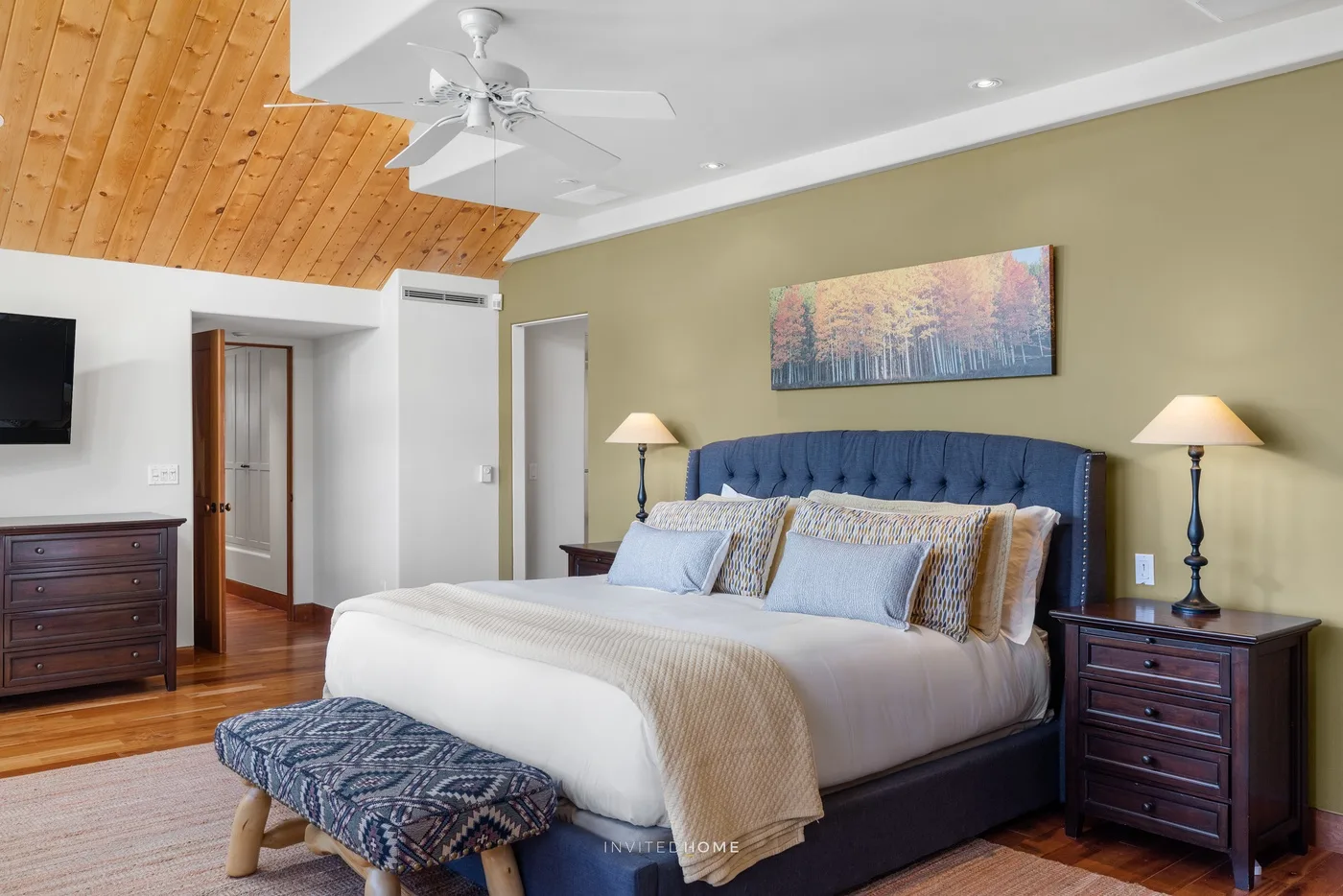 Un dormitorio con una cama grande, cabecero tapizado azul y techo inclinado de madera.