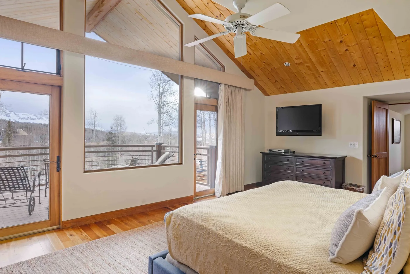 Un dormitorio con una cama, un televisor en la pared y grandes ventanas con vistas a un paisaje nevado.