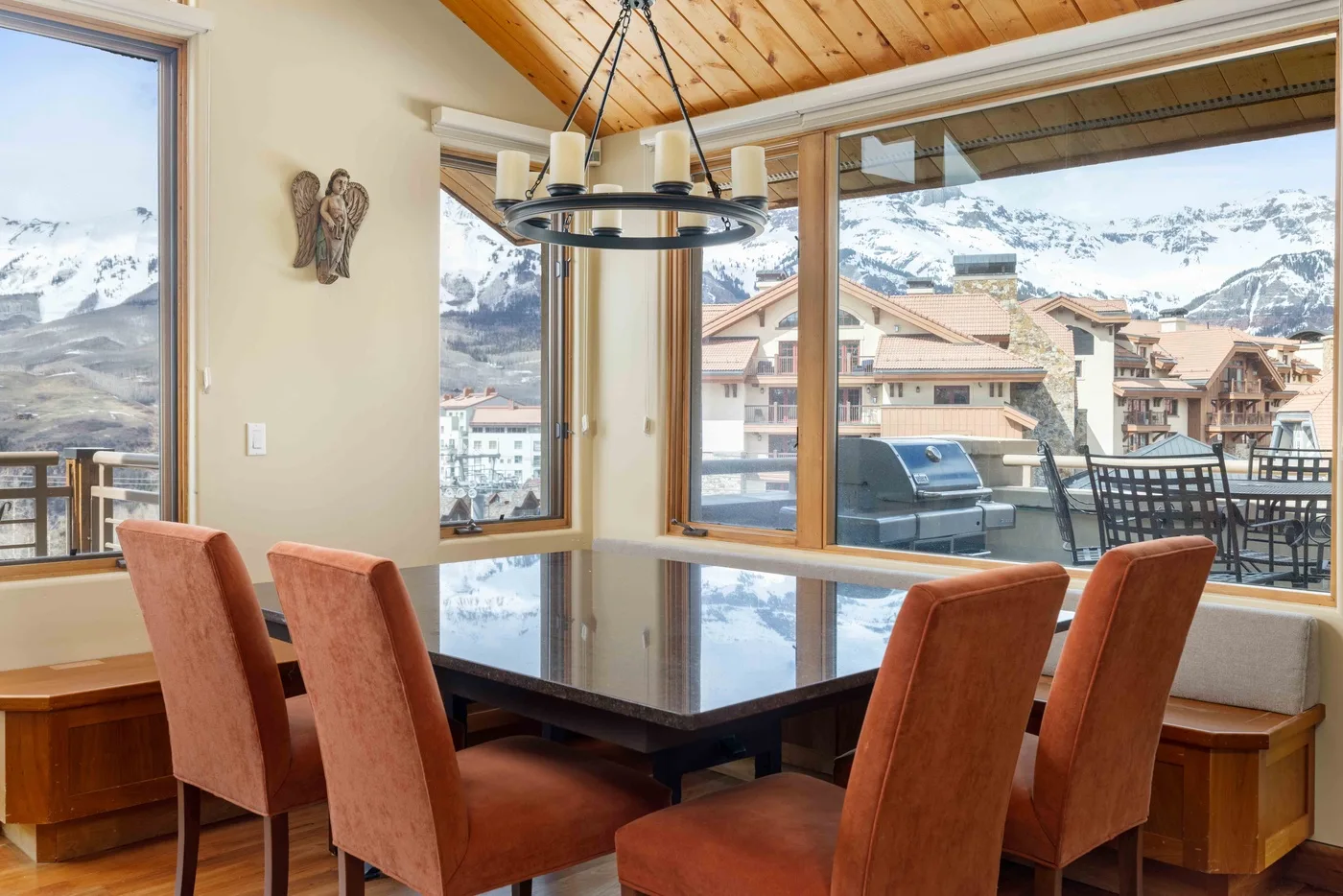 Comedor con mesa y asientos junto a grandes ventanas con vistas a montañas nevadas.