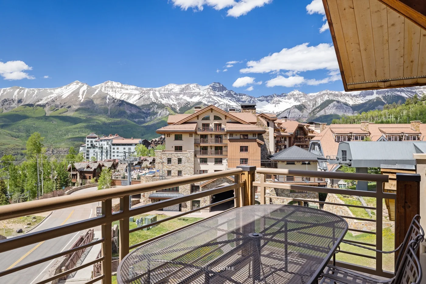 Un balcón con asientos al aire libre ofrece vistas de edificios cercanos y montañas nevadas.